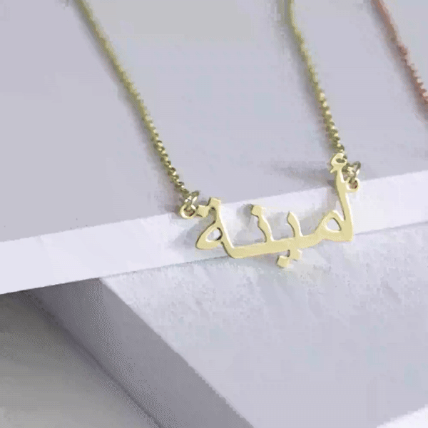 Gold custom Arabic name necklace laying on a white surface, showcasing personalized jewelry design for unique and elegant fashion accessories.