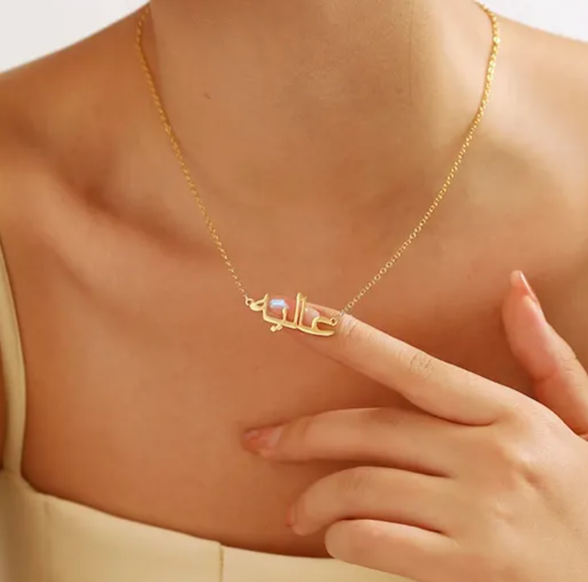 Woman wearing a custom Arabic name necklace in gold, with her finger touching the necklace, highlighting personalized jewelry for unique and stylish fashion accessories.