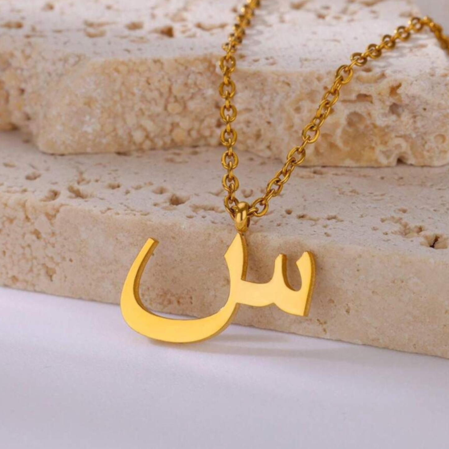 Gold Letter necklace with a unique pendant on a textured surface