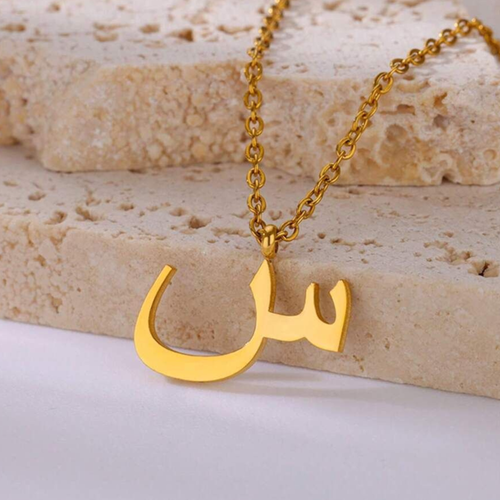 Gold Letter necklace with a unique pendant on a textured surface