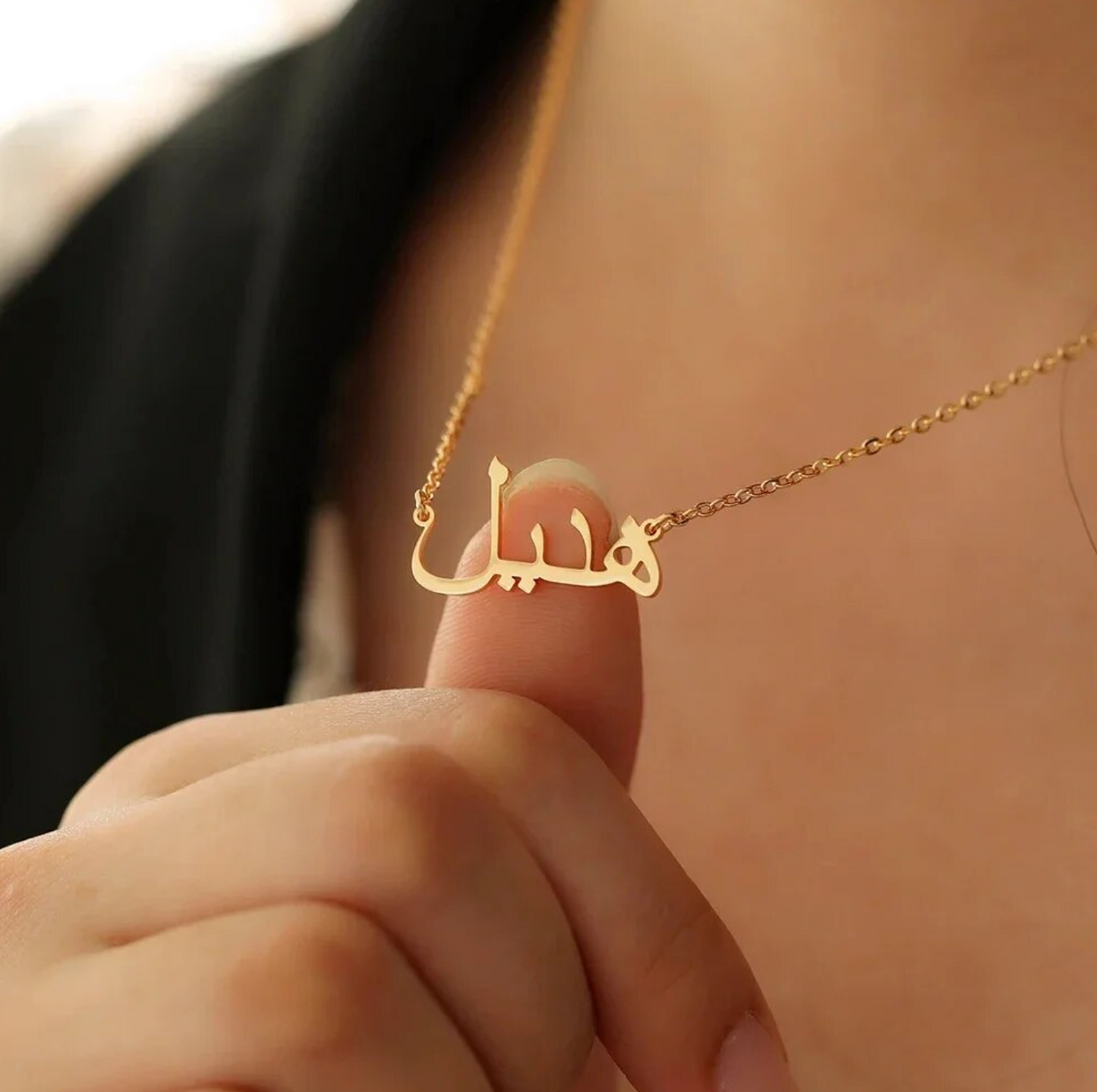 Closeup of a woman holding a custom Arabic name necklace in gold, showcasing personalized jewelry design for unique and stylish fashion accessories.