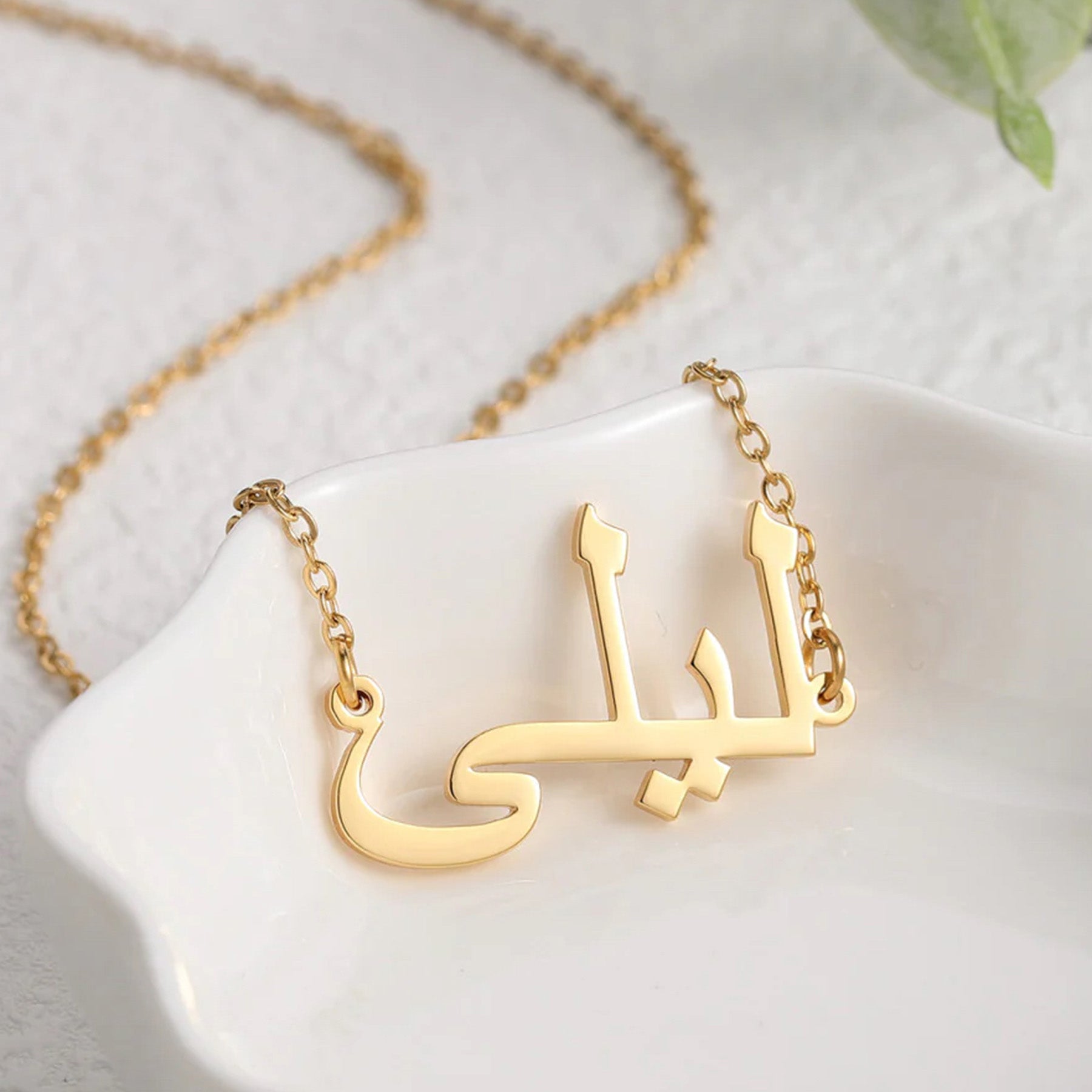 Custom Arabic name necklace in gold, elegantly placed in a white dish, showcasing personalized jewelry design for stylish and unique fashion accessories.