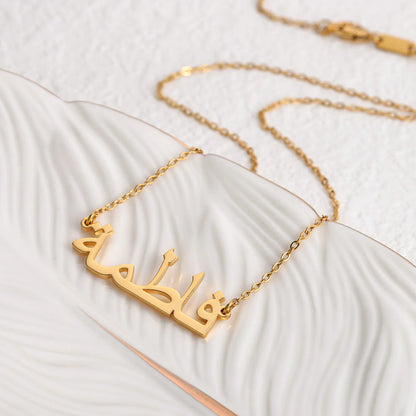 Custom Arabic name necklace in gold, elegantly displayed on a white dish with a textured design, showcasing personalized jewelry for stylish and unique fashion accessories.