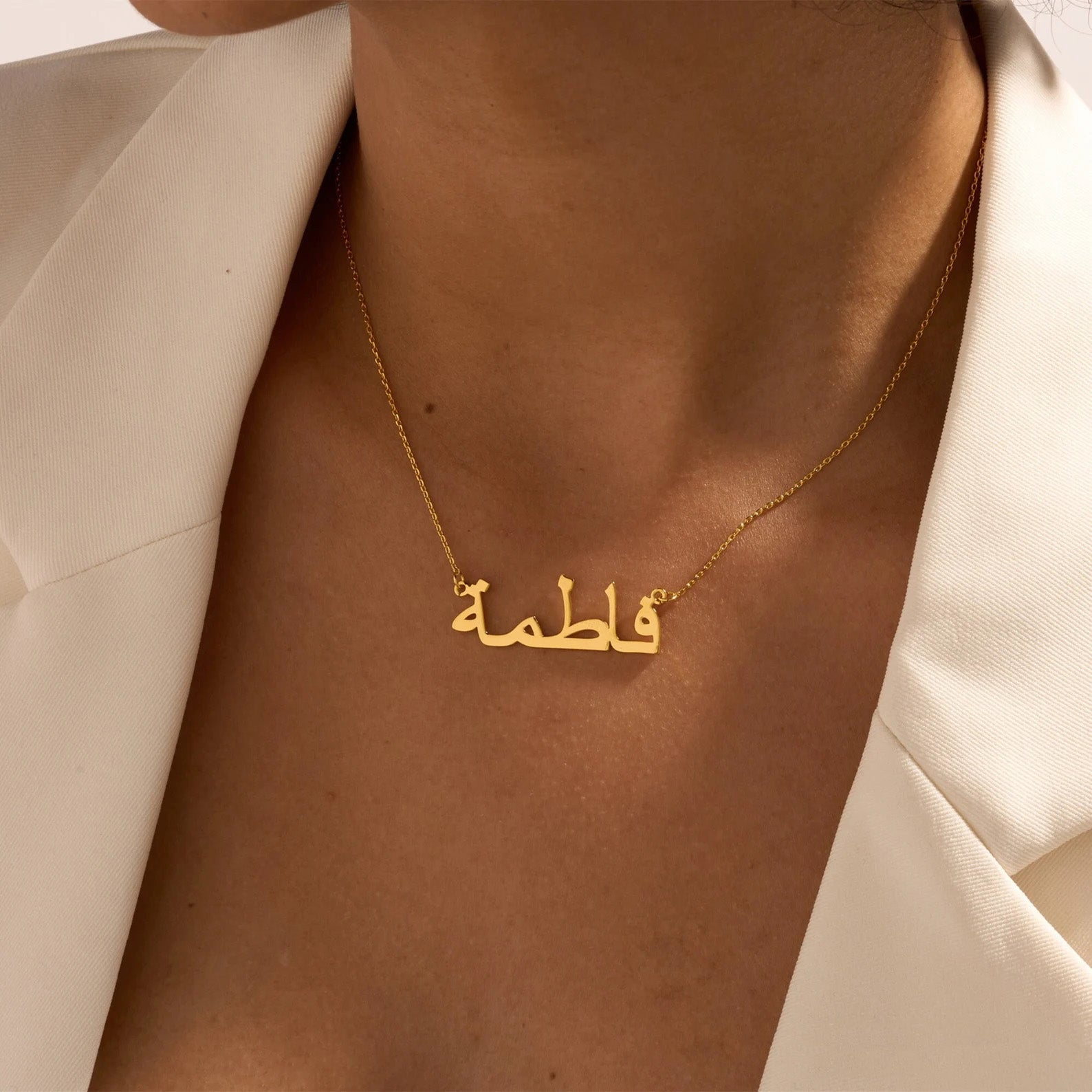 Woman wearing a custom Arabic name necklace in gold, displayed against a white outfit, highlighting personalized jewelry for stylish fashion accessories.