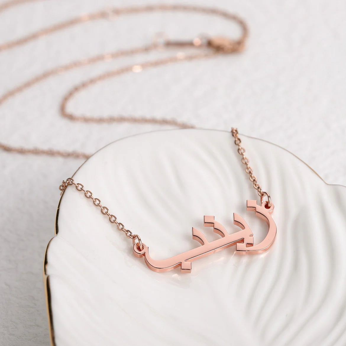 Custom Arabic name necklace in rose gold, elegantly displayed on a white dish, showcasing personalized jewelry design for stylish and unique fashion accessories.