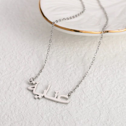 Custom Arabic name necklace in silver, elegantly displayed on a white dish with a gold rim, showcasing personalized jewelry for stylish and unique fashion accessories.