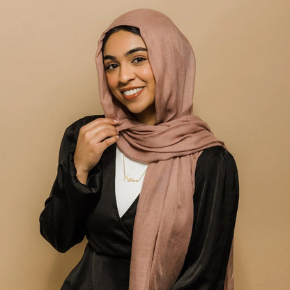 Smiling woman wearing a custom Arabic name necklace in gold, paired with a hijab and a black outfit, highlighting personalized jewelry for elegant fashion accessories.