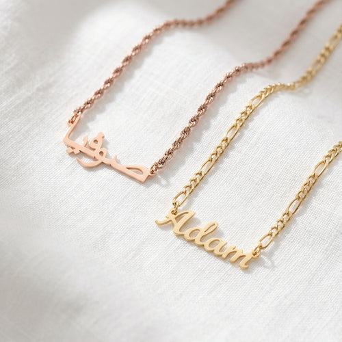 Rose gold Arabic name necklace on twisted rope chain and gold English name necklace on figaro chain flat lay